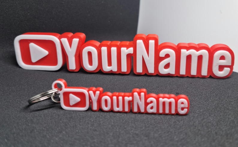 Puede incluir: Llavero impreso en 3D rojo y blanco con un bot&oacute;n de reproducci&oacute;n y el texto "YourName".