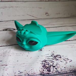 Op de afbeelding: Een 3D-geprint beeldje van een personage met grote oren en ogen, gemaakt van turquoisegroen plastic. Het beeldje is een populair personage uit een sciencefictionfilm.