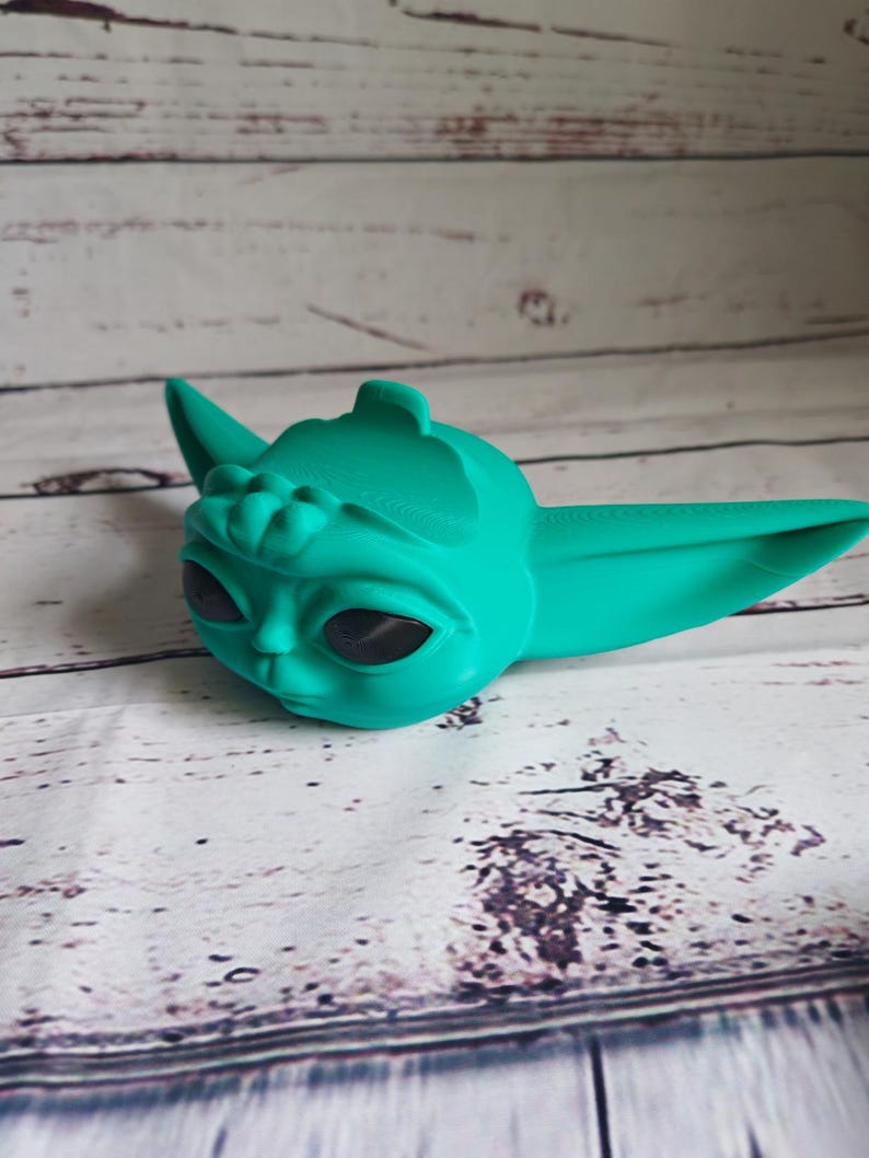 Op de afbeelding: Een 3D-geprint beeldje van een personage met grote oren en ogen, gemaakt van turquoisegroen plastic. Het beeldje is een populair personage uit een sciencefictionfilm.