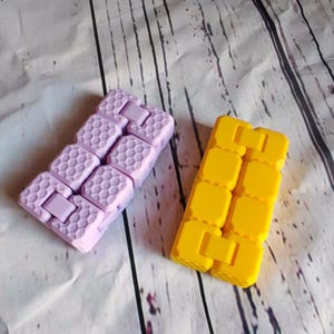 Peut inclure: Deux jouets anti-stress, l'un violet et l'autre jaune, en silicone. Le jouet violet a un motif en nid d'abeille et le jouet jaune a un motif carr&eacute;.