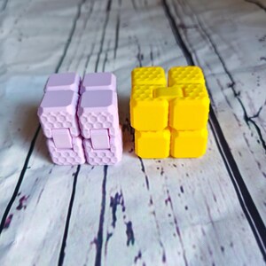 Peut inclure: Deux jouets anti-stress, l'un est jaune et l'autre est violet. Les deux sont en plastique et ont un motif en nid d'abeille.