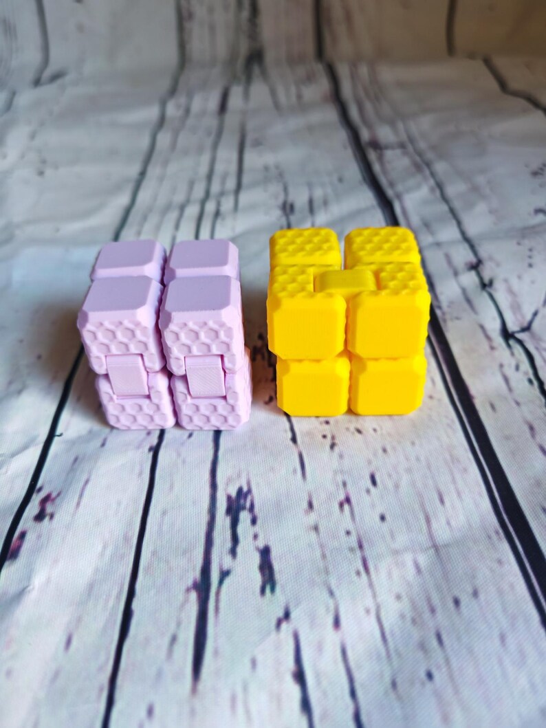 Peut inclure: Deux jouets anti-stress, l'un est jaune et l'autre est violet. Les deux sont en plastique et ont un motif en nid d'abeille.