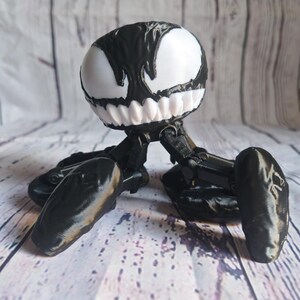 May include: Black and white 3D printed figurine of a Venom character with a large head and four legs.