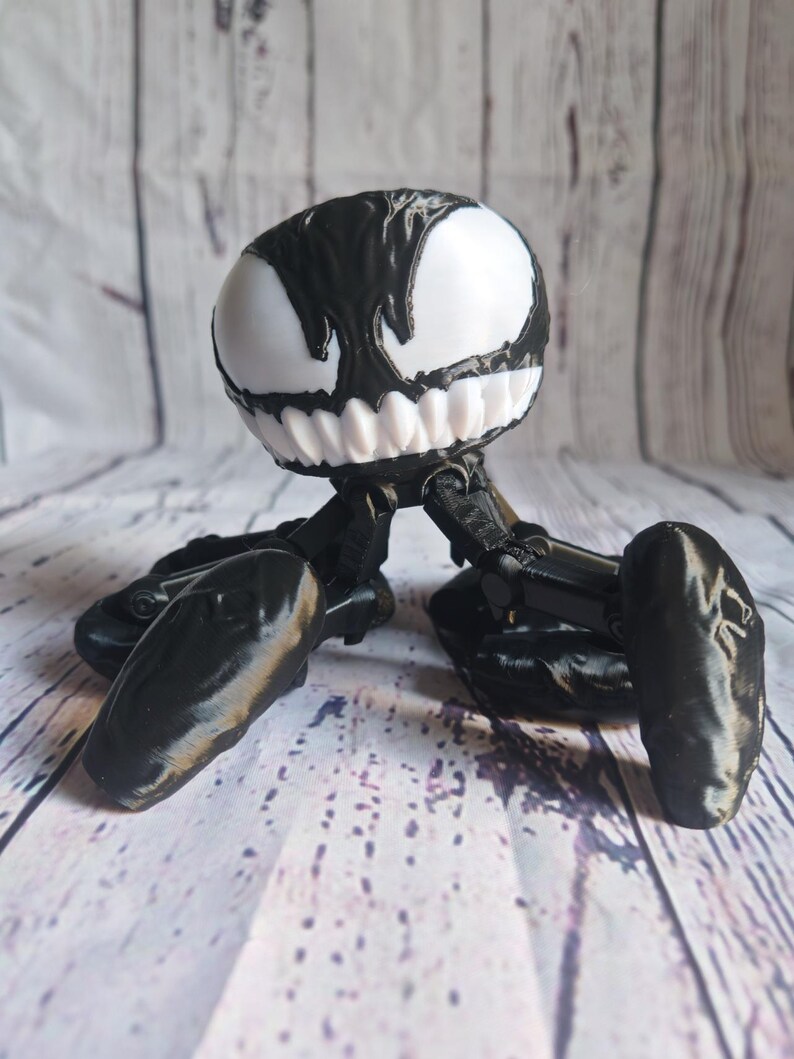 May include: Black and white 3D printed figurine of a Venom character with a large head and four legs.