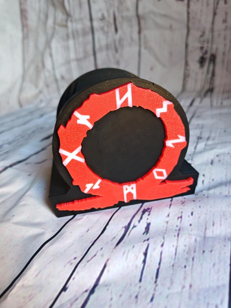 Peut inclure: Objet imprim&eacute; en 3D noir et rouge en forme de cercle avec des runes autour du bord. Les runes sont blanches et le cercle est rouge. L'objet est sur une surface en bois blanc.
