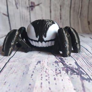 May include: A black and white 3D printed figurine of Venom from the Marvel comics, depicted as a spider with a menacing grin.