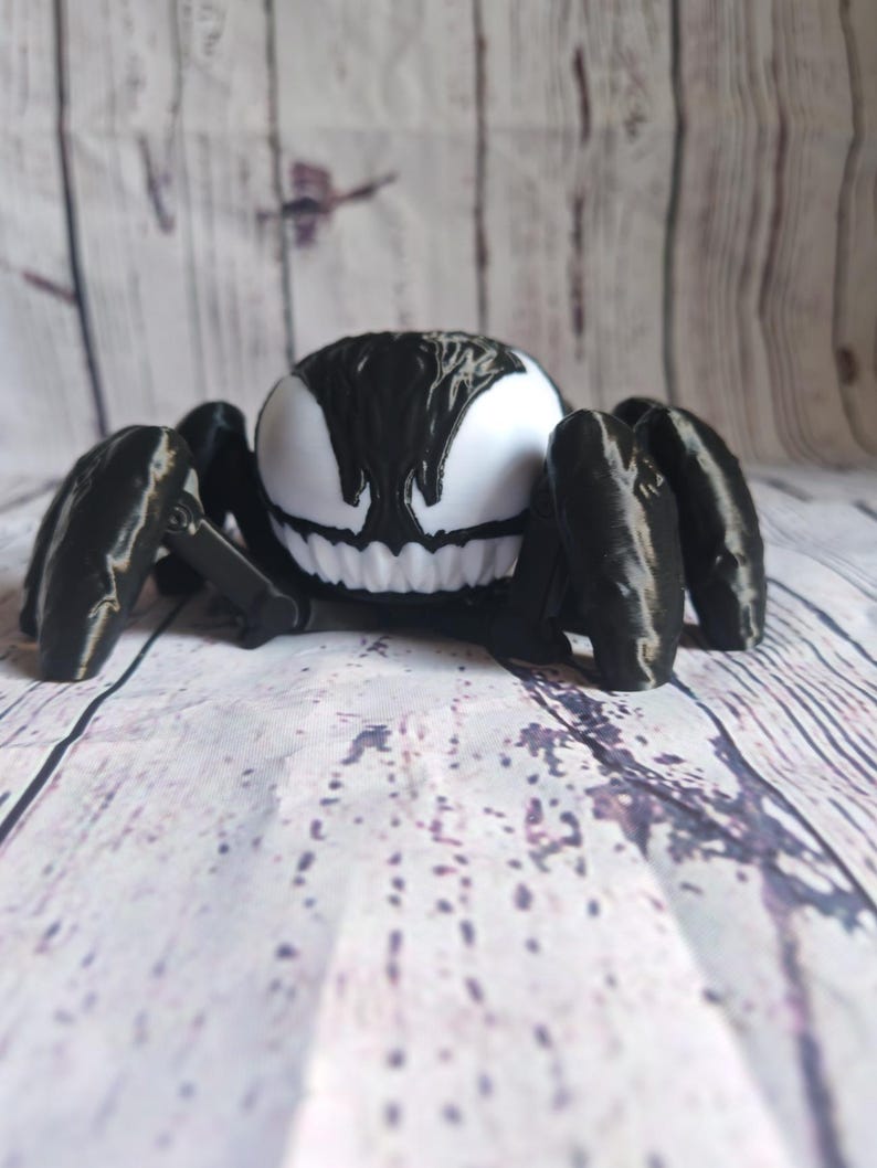 May include: A black and white 3D printed figurine of Venom from the Marvel comics, depicted as a spider with a menacing grin.