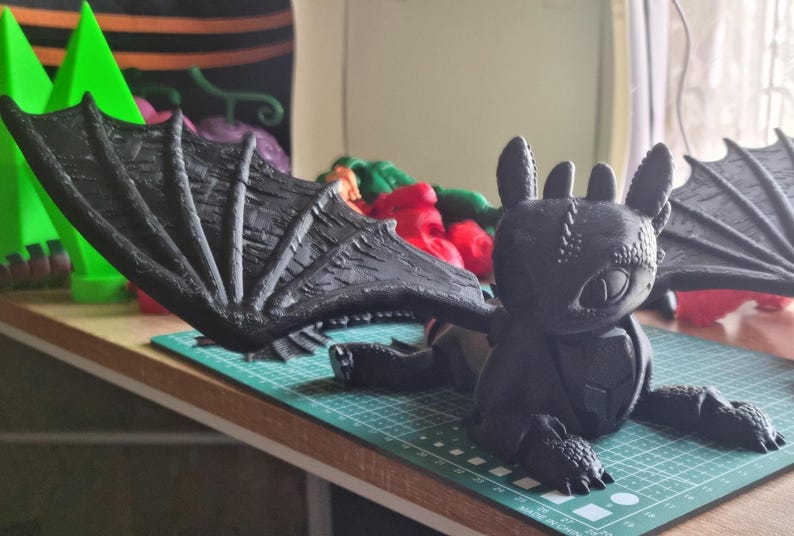 May include: A black 3D printed dragon figurine with large wings. The dragon has a textured surface and a detailed face.