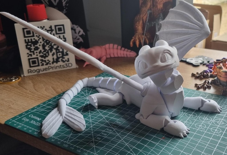 May include: A white 3D printed model of a dragon with wings outstretched. The dragon is posed on its belly with its head raised. The model is printed in multiple pieces and is ready to be assembled.