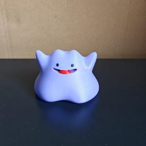 以下が含まれることがあります： ゲンガーと呼ばれるポケモンのキャラクターの紫と赤のプラスチック製フィギュア。キャラクターは大きく笑っており、赤い舌が突き出ています。