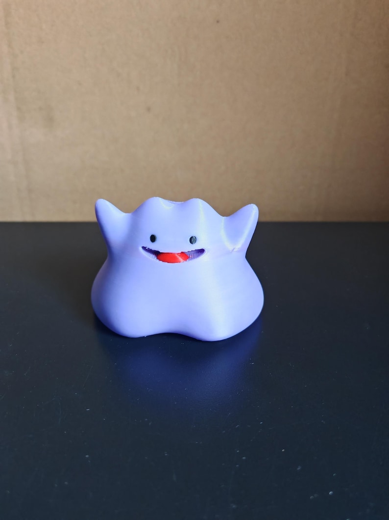 以下が含まれることがあります： ゲンガーと呼ばれるポケモンのキャラクターの紫と赤のプラスチック製フィギュア。キャラクターは大きく笑っており、赤い舌が突き出ています。
