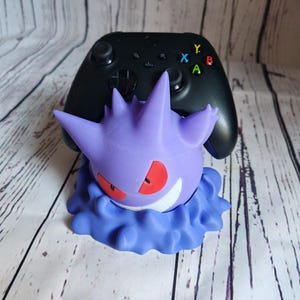 Könnte beinhalten: Ein lila und blauer 3D-gedruckter Videospiel-Controller-Ständer mit einem Gengar-Pokémon-Design.