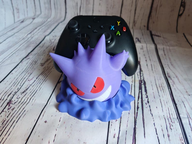 Może przedstawiać: Stojak na kontroler do gier wideo, wydrukowany w 3D, w kolorze fioletowym i niebieskim, z wzorem Pokemona Gengar.