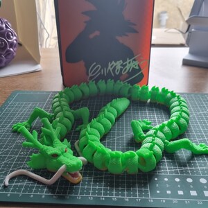 Op de afbeelding: Een groene drakenfiguur met een witte onderkant, gemaakt van gesegmenteerde stukken, die lijkt op een populair anime-personage. De draak is in een opgerolde positie op een groene snijmat geplaatst.