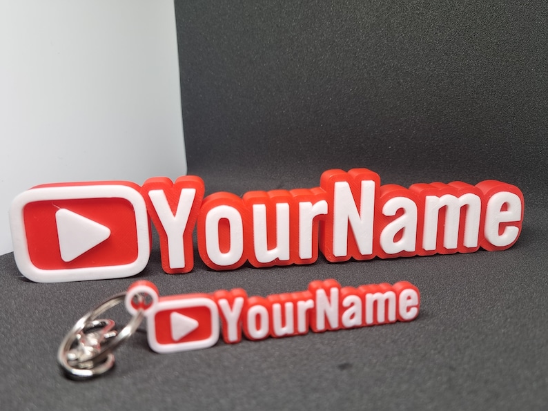 Puede incluir: Llavero de pl&aacute;stico rojo y blanco con un bot&oacute;n de reproducci&oacute;n y el texto "YourName".