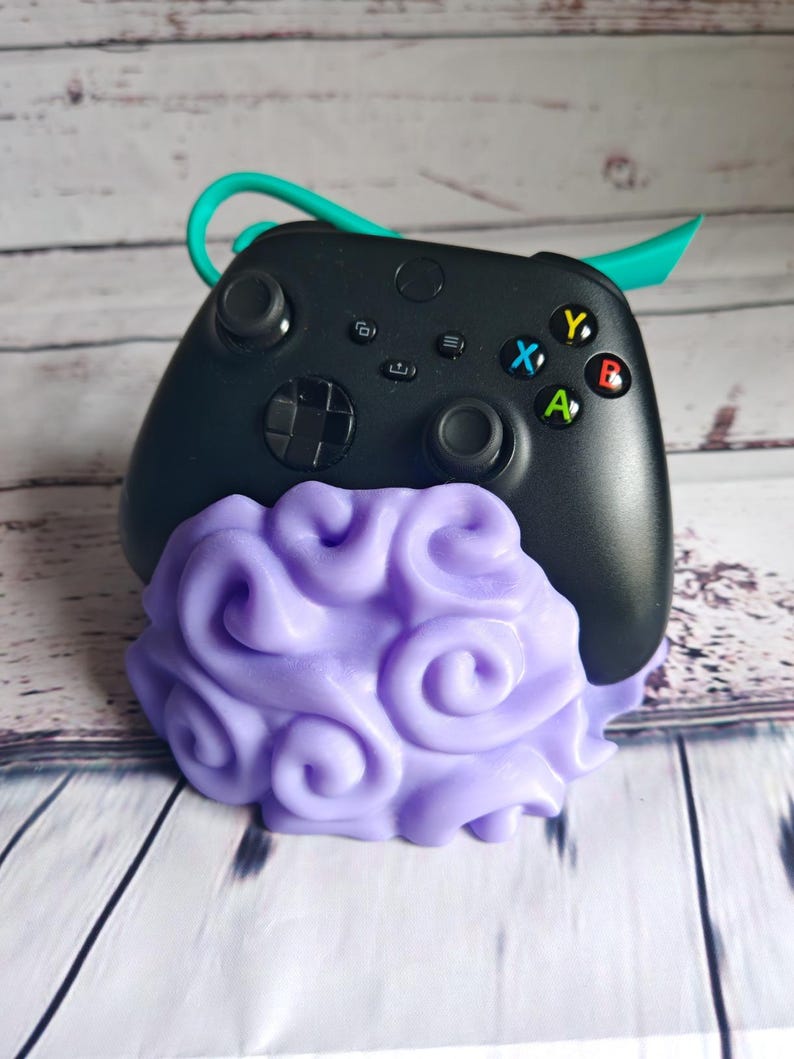 Op de afbeelding: Een zwarte videogamecontroller met een paarse, wervelvormige standaard. De controller heeft een groene band.