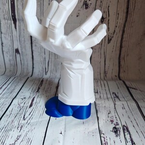 K&ouml;nnte beinhalten: Eine wei&szlig;e, 3D-gedruckte Handskulptur mit einem blauen Sockel. Die Hand ist in einer Greifbewegung dargestellt, wobei die Finger nach innen gekr&uuml;mmt sind.