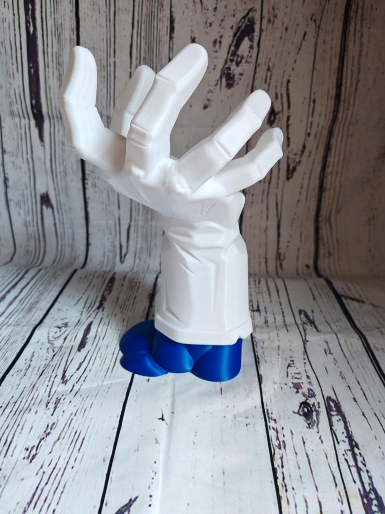 K&ouml;nnte beinhalten: Eine wei&szlig;e, 3D-gedruckte Handskulptur mit einem blauen Sockel. Die Hand ist in einer Greifbewegung dargestellt, wobei die Finger nach innen gekr&uuml;mmt sind.