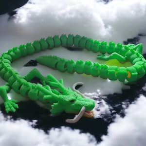 Op de afbeelding: Een groen gesegmenteerd draken speelgoed met een lange staart en een kop met witte tanden. Het speelgoed is gemaakt van flexibel plastic en is in een gekromde positie geplaatst.