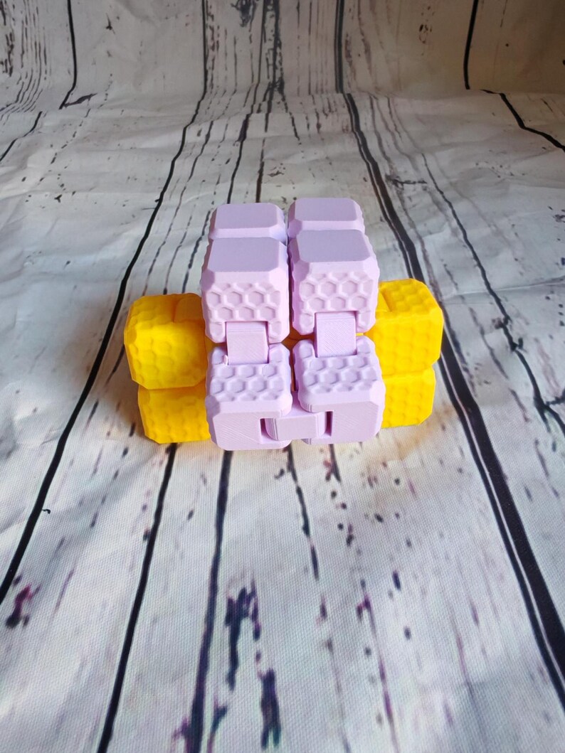Peut inclure: Un jouet anti-stress rose et jaune avec un motif en nid d'abeille. Le jouet est en plastique et a une forme carr&eacute;e.