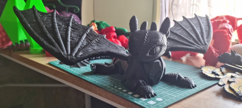 K&ouml;nnte beinhalten: Eine schwarze, 3D-gedruckte Drachenfigur mit gro&szlig;en Fl&uuml;geln, einem strukturierten K&ouml;rper und einem detaillierten Gesicht. Der Drache sitzt auf einer gr&uuml;nen Schneidematte.