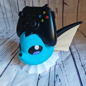 May include: A blue and white Pokemon character figurine with a white base. A black Xbox controller is sitting on top of the figurine.