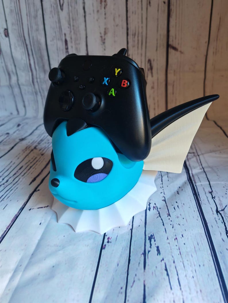 May include: A blue and white Pokemon character figurine with a white base. A black Xbox controller is sitting on top of the figurine.