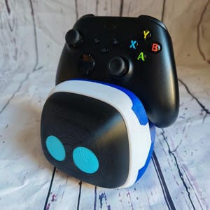 Op de afbeelding: Een zwart-witte gaming-headset met blauwe accenten zit bovenop een zwarte Xbox-controller. De headset heeft twee blauwe ronde lampjes aan de voorkant.