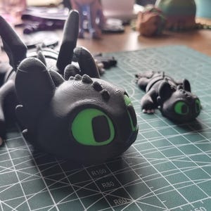 May include: Two black and green dragon figurines. The larger dragon is lying down with its wings spread out. The smaller dragon is standing up with its wings folded. Both dragons have green eyes.