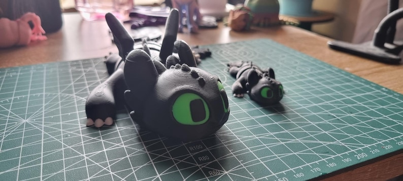 May include: Two black and green dragon figurines. The larger dragon is lying down with its wings spread out. The smaller dragon is standing up with its wings folded. Both dragons have green eyes.