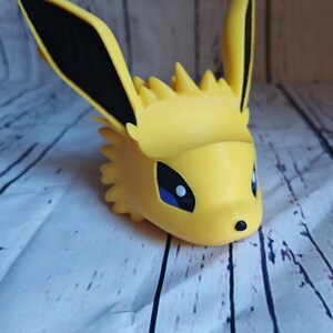Peut inclure: Une figurine en 3D imprim&eacute;e en jaune d'un personnage Pokemon avec des oreilles noires et des yeux bleus. La figurine est un portrait du personnage.