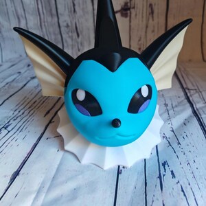 May include: A blue and black 3D printed figurine of a Pokemon character with a white collar. The character has a pointed fin on its head and large ears.
