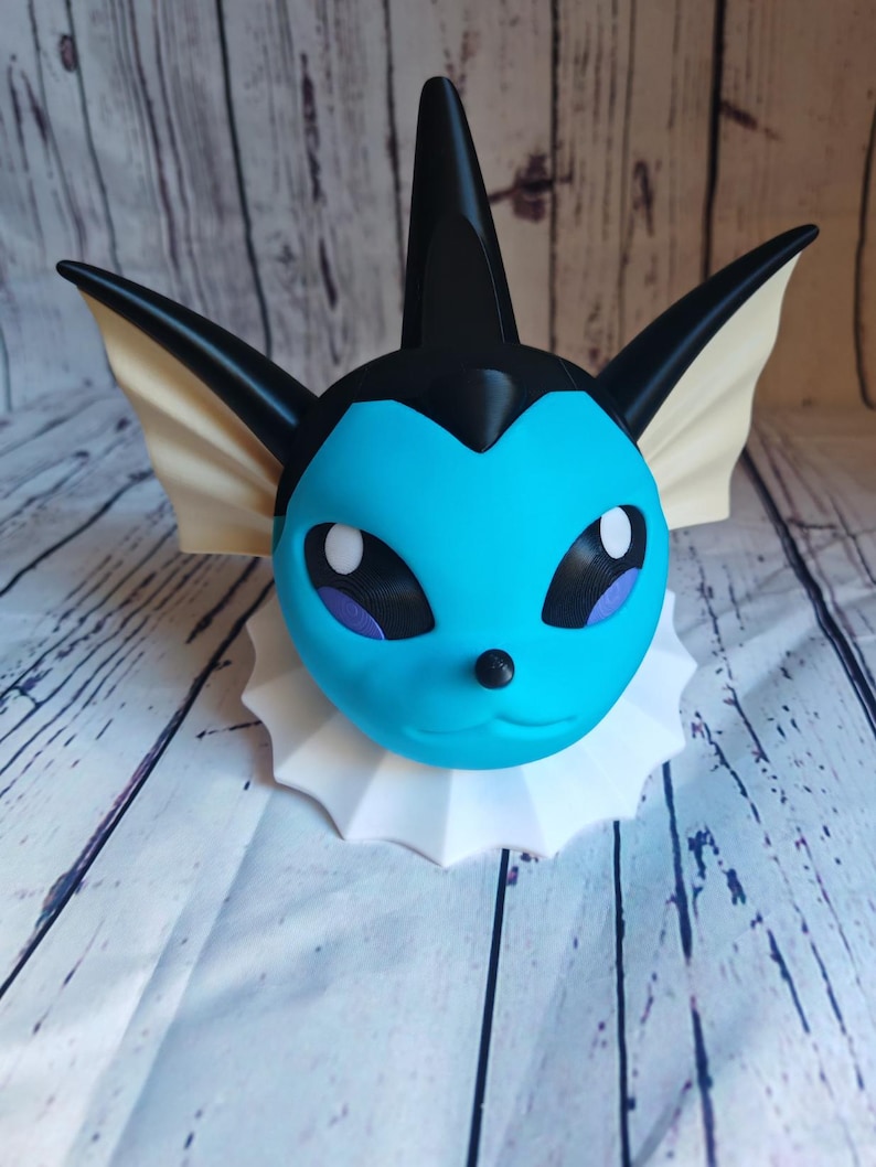 May include: A blue and black 3D printed figurine of a Pokemon character with a white collar. The character has a pointed fin on its head and large ears.