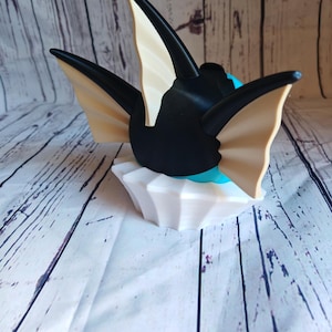 May include: A black and white 3D printed figurine of a Pokemon character with large, pointed ears. The figurine is sitting on a white base.