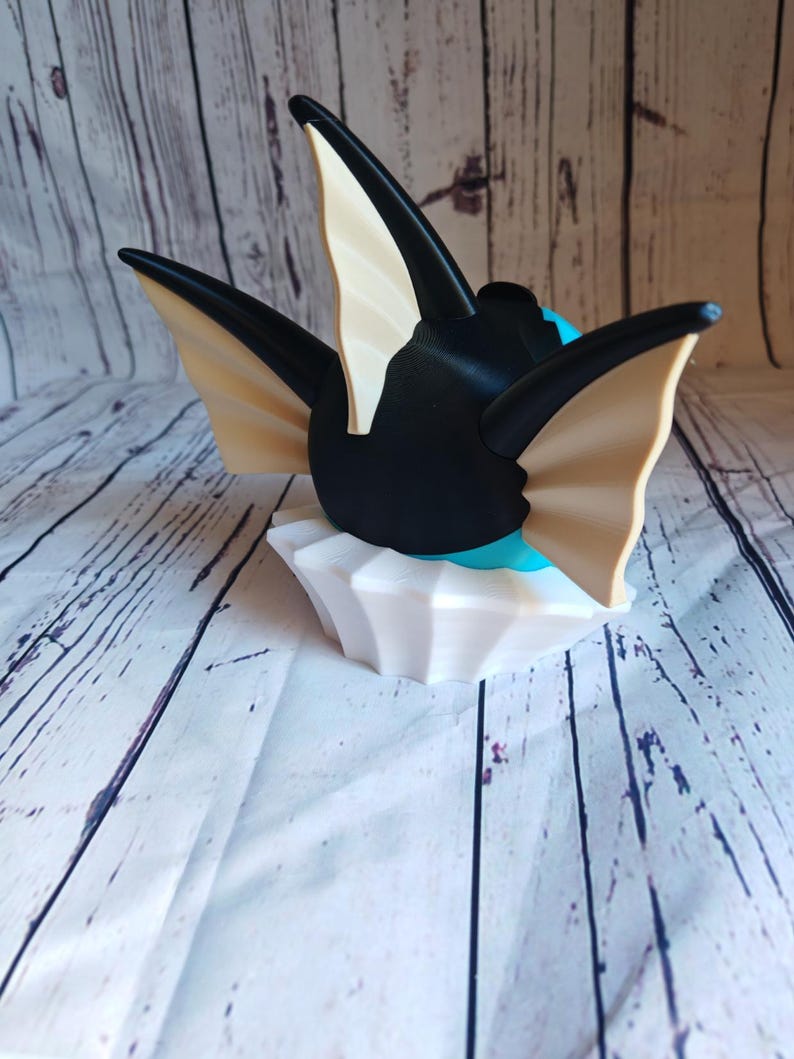 May include: A black and white 3D printed figurine of a Pokemon character with large, pointed ears. The figurine is sitting on a white base.
