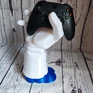 Könnte beinhalten: Eine weiße, im 3D-Druck hergestellte Hand hält einen schwarzen Xbox-Controller. Die Hand steht auf einem blauen Sockel.