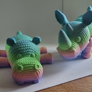 May include: Two crocheted animal figurines, a pink and green hippopotamus and a blue and green rhinoceros, both with rainbow coloured yarn.