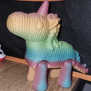 May include: A rainbow crocheted unicorn toy with a textured surface. The unicorn has a horn, mane, and tail.