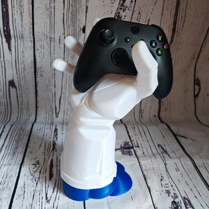 K&ouml;nnte beinhalten: Eine wei&szlig;e, im 3D-Druck hergestellte Hand h&auml;lt einen schwarzen Xbox-Controller. Die Hand hat eine blaue Basis.