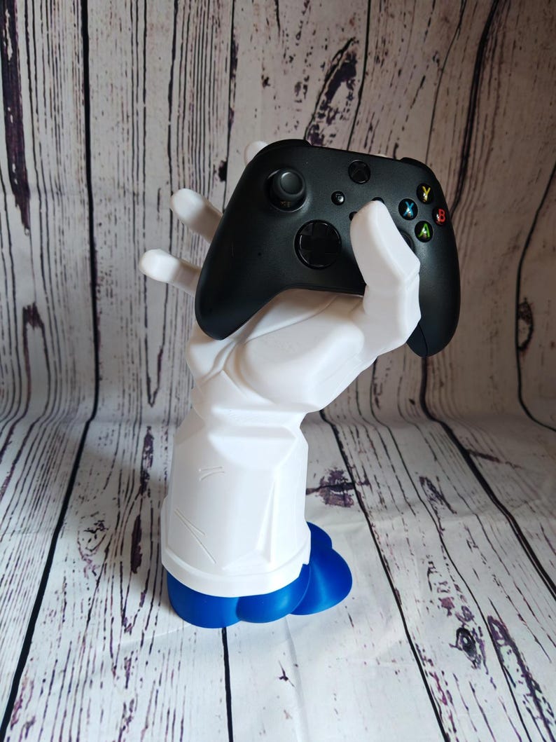 K&ouml;nnte beinhalten: Eine wei&szlig;e, im 3D-Druck hergestellte Hand h&auml;lt einen schwarzen Xbox-Controller. Die Hand hat eine blaue Basis.