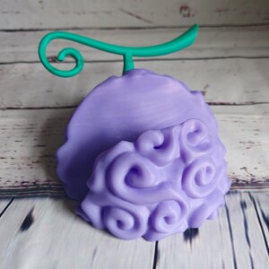 Op de afbeelding: Een 3D-geprint figuurtje van een vrucht in paars en groen met een swirl-patroon. De vrucht heeft een groene steel met een gekruld uiteinde.