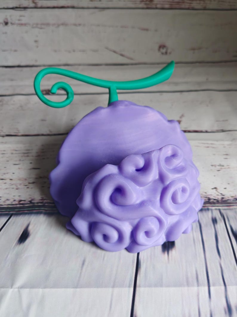 Op de afbeelding: Een 3D-geprint figuurtje van een vrucht in paars en groen met een swirl-patroon. De vrucht heeft een groene steel met een gekruld uiteinde.