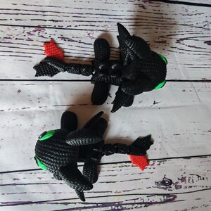 May include: Two black crocheted dragon figurines with green eyes and red tails. The dragons are posed in a flying position.