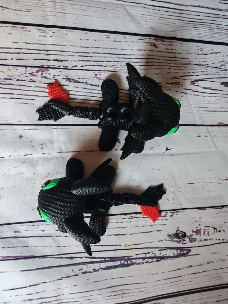 May include: Two black crocheted dragon figurines with green eyes and red tails. The dragons are posed in a flying position.