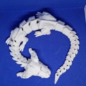 Op de afbeelding: Witte 3D-geprinte drakenfiguur met een gesegmenteerde staart en een gedetailleerd hoofd. De draak is opgerold in een cirkel.