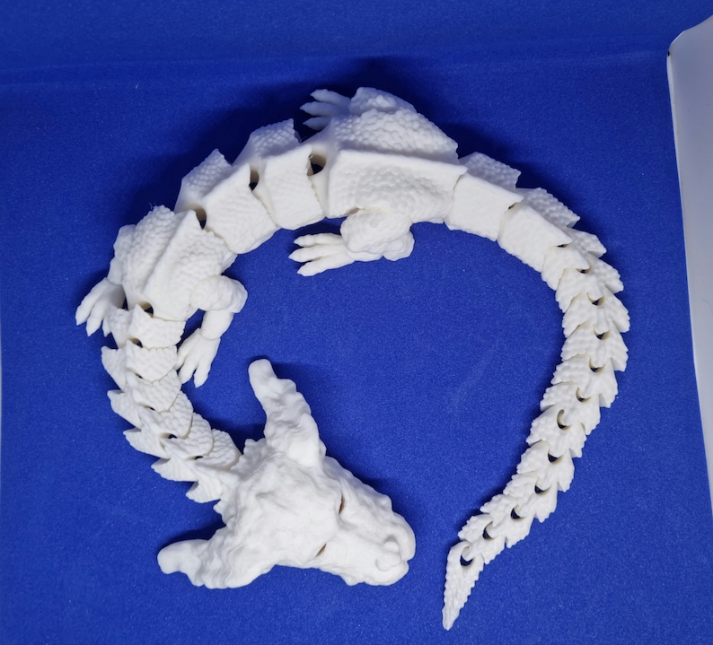 Op de afbeelding: Witte 3D-geprinte drakenfiguur met een gesegmenteerde staart en een gedetailleerd hoofd. De draak is opgerold in een cirkel.