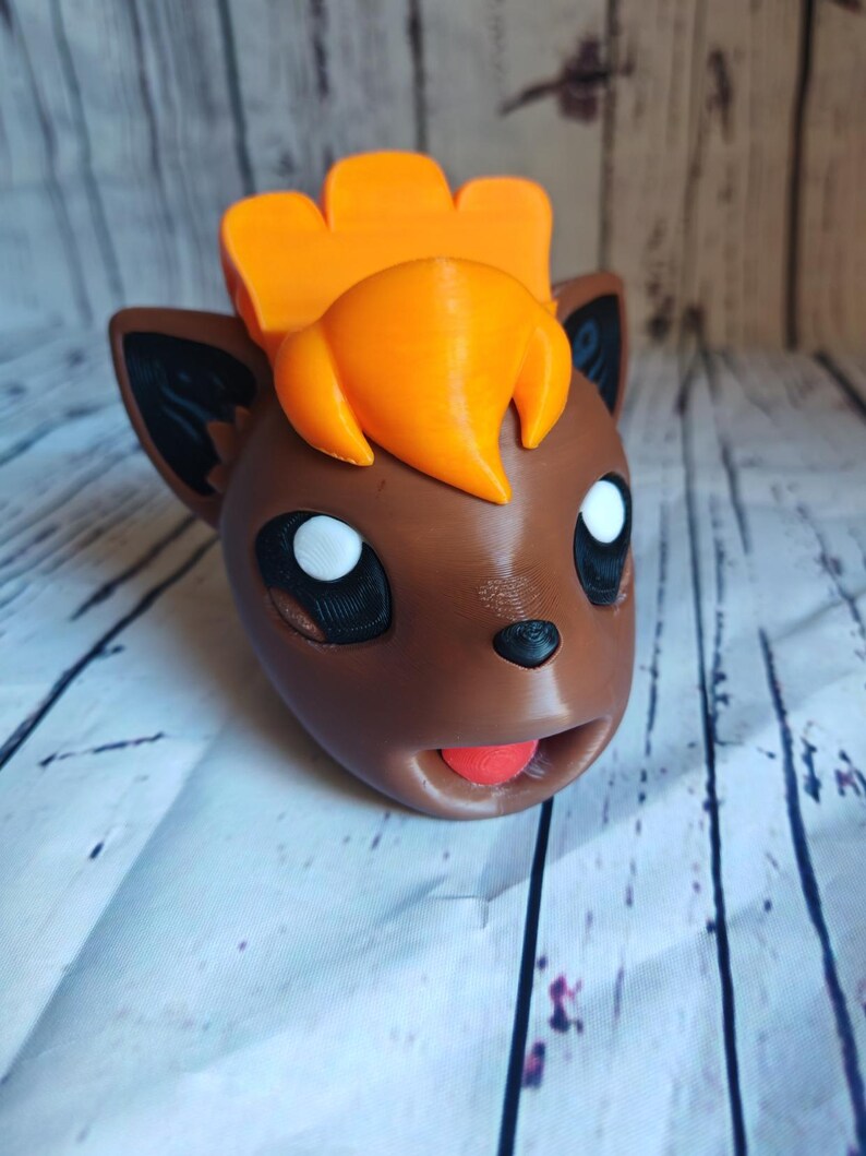 Pode incluir: Uma figura de Pokemon impressa em 3D de cor marrom e laranja com uma grande juba laranja e uma l&iacute;ngua vermelha que se projeta.