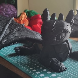 K&ouml;nnte beinhalten: Eine schwarze, 3D-gedruckte Drachenfigur mit ausgebreiteten Fl&uuml;geln. Der Drache hat eine strukturierte Oberfl&auml;che und ein detailliertes Gesicht. Die Figur steht auf einer gr&uuml;nen Schneidematte.