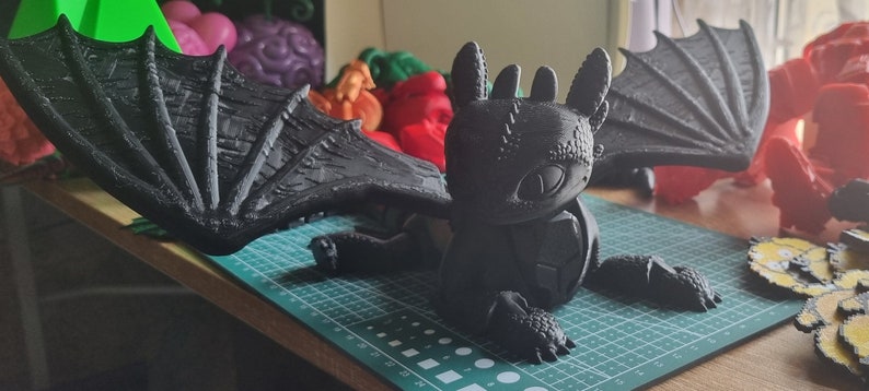 K&ouml;nnte beinhalten: Eine schwarze, 3D-gedruckte Drachenfigur mit ausgebreiteten Fl&uuml;geln. Der Drache hat eine strukturierte Oberfl&auml;che und ein detailliertes Gesicht. Die Figur steht auf einer gr&uuml;nen Schneidematte.