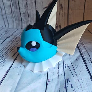 May include: A blue and black 3D printed figurine of a Pokemon character with a white collar. The figurine is posed with its head tilted to the side.